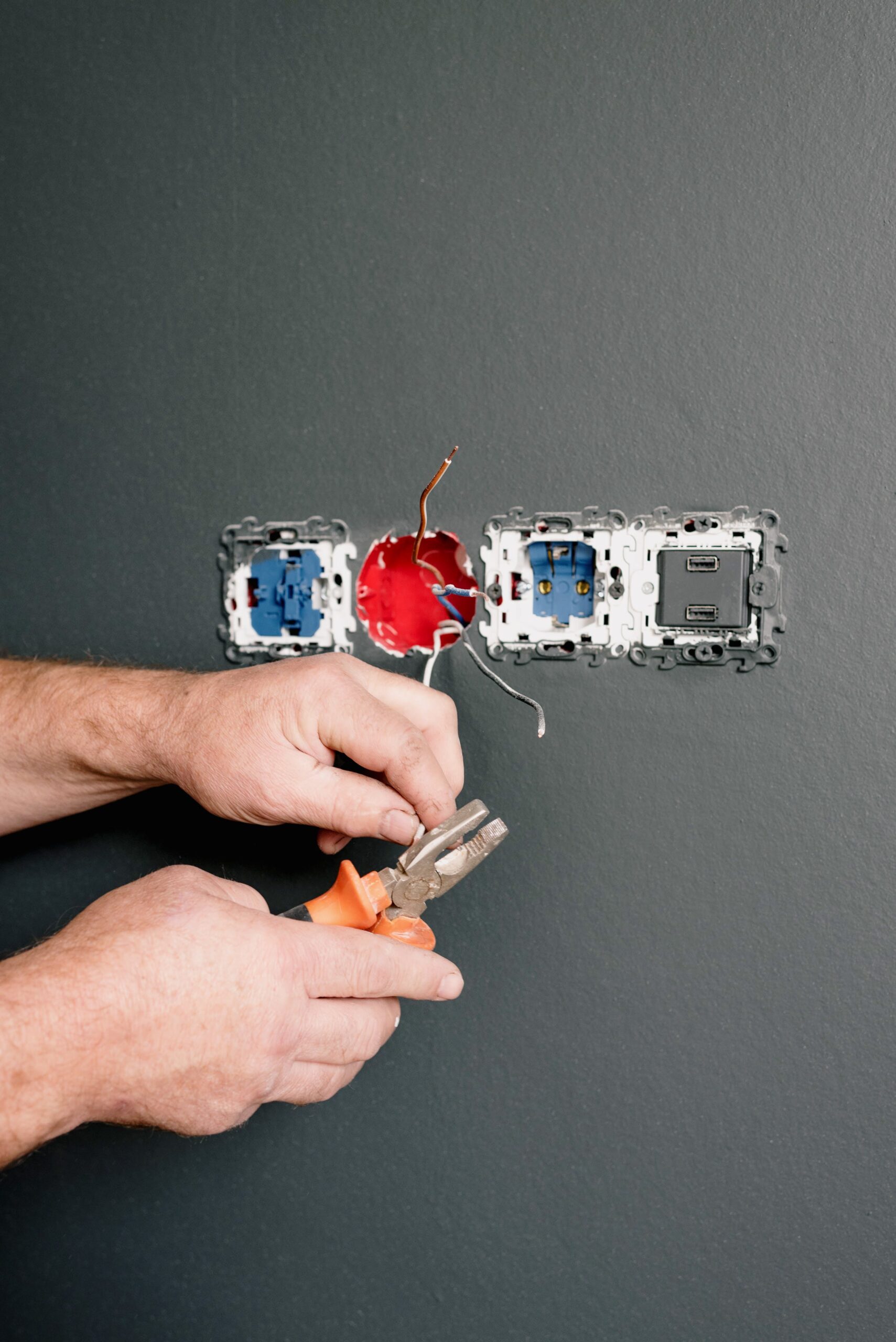 Crop faceless electrician using pliers for installation sockets and switches in new apartment